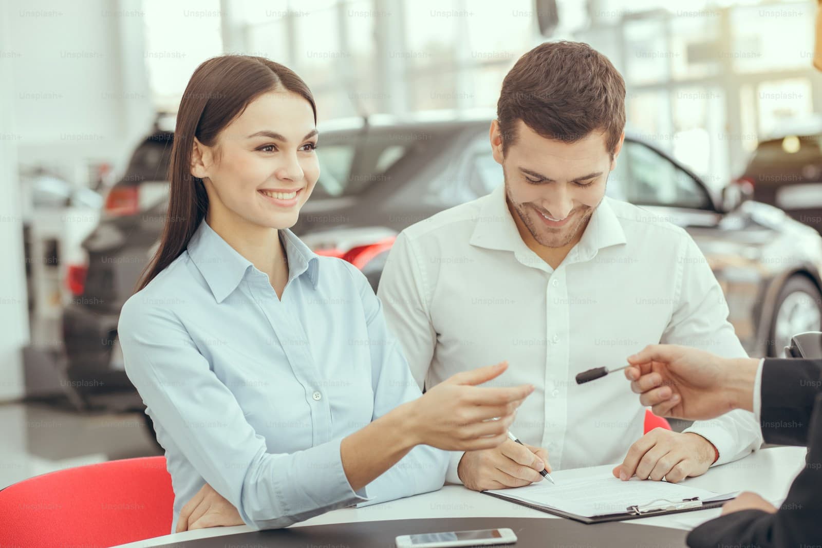 Couple signing paperwork at a table in a car dealership showroom