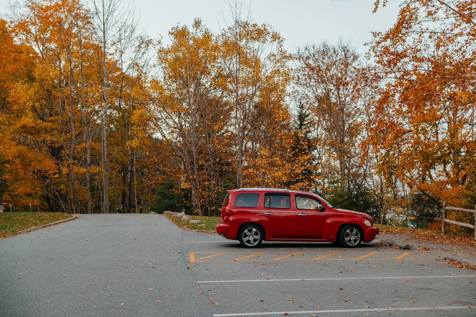Red vintage van parked on road surrounded by orange and yellow autumn trees