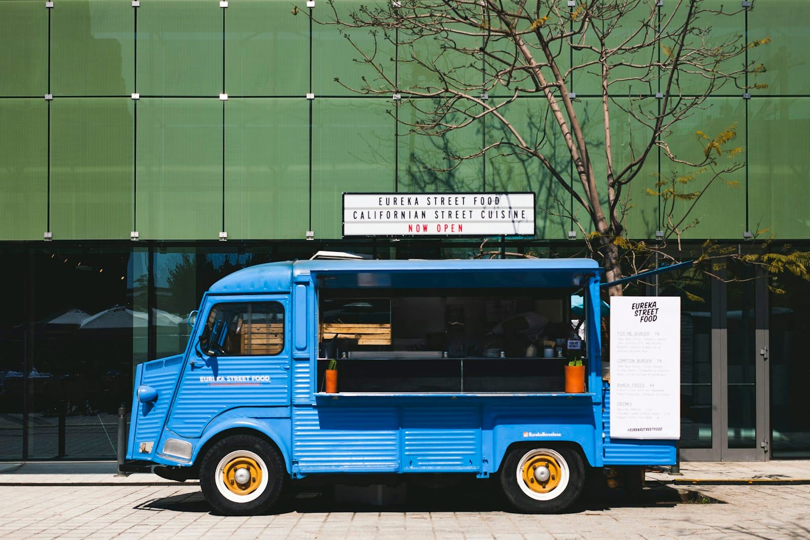 Bright blue vintage-style food truck parked outside a modern glass building